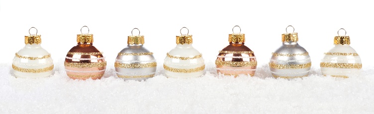 Christmas border of shiny white, gold and silver baubles resting in snow over a white background