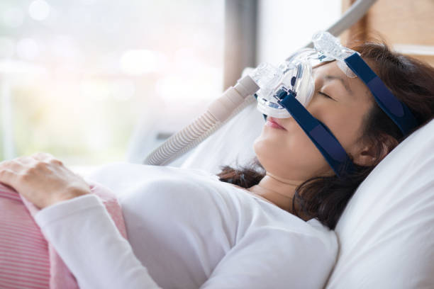 Woman and cpap mask, healthcare concept. Senior woman using cpap machine to stop choking and snoring from obstructive sleep apnea with bokeh and morning light background. sleep apnea photos stock pictures, royalty-free photos & images