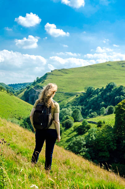 Woman looking at the hills in the English Peak District National Park on a summer day with blue sky The photo was taken in Dovedale in Derbyshire, England, UK. The blond woman is visable out of a rear view. bakewell photos stock pictures, royalty-free photos & images