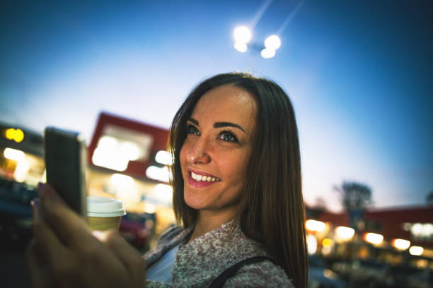 istock Smiling young woman using smart phone on streets by night 864408386