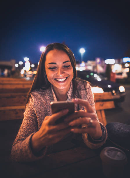 istock Smiling young woman using smart phone on streets by night 864408876