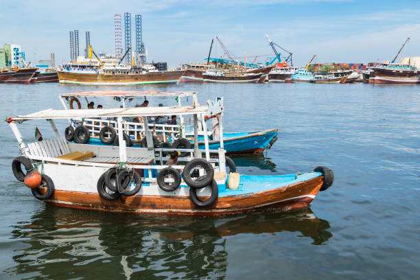 Water taxi with commuters, arriving to the Sharjah Corniche, with arabic style vessels and Port Khalid in the background