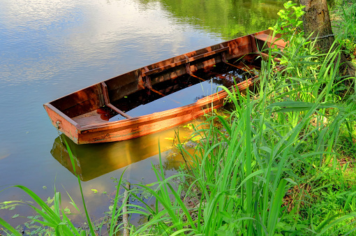 A red orange wooden boat sits on a lake, filling with water