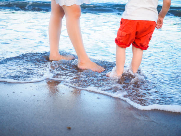 Mother and son playing in spuming water with wave on beach at summer