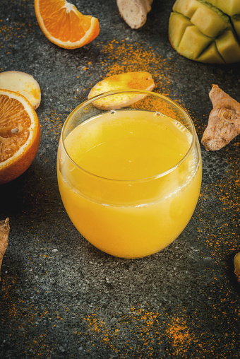 Indian cuisine recipes. Healthy food, detox water. Traditional Indian mango, orange, turmeric and ginger smoothie, on a dark stone table. Copy space