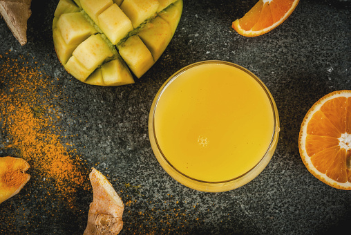 Indian cuisine recipes. Healthy food, detox water. Traditional Indian mango, orange, turmeric and ginger smoothie, on a dark stone table. Copy space top view