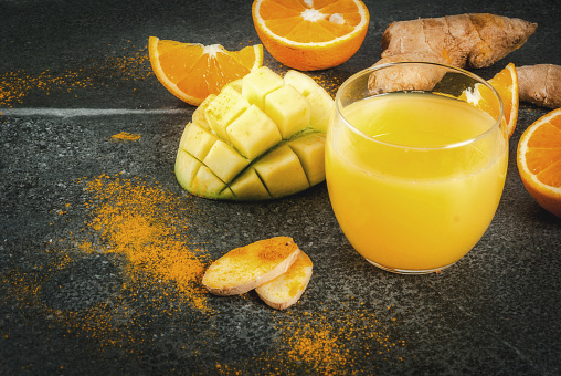 Indian cuisine recipes. Healthy food, detox water. Traditional Indian mango, orange, turmeric and ginger smoothie, on a dark stone table. Copy space