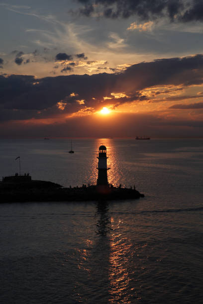 Moody sunset over lighthouse at shore in ocean