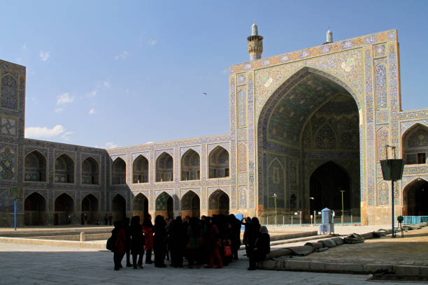 It's a peaceful day at Imam Square (Naqsh-e Jahan Square) as visitors take a leisurely stroll amidst the lush greenery. The historic buildings in the background add to the charm. Isfahan, Iran.