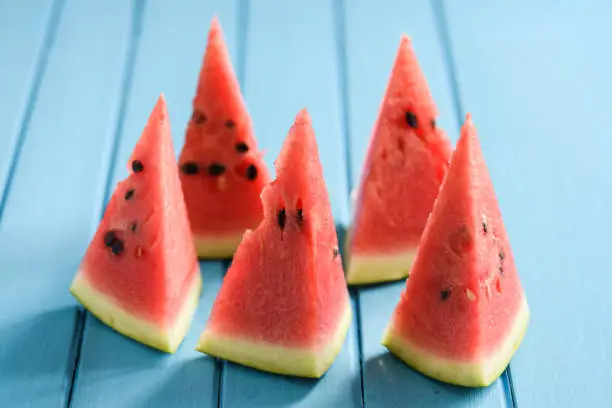 Bright red watermelon slices on blue background looking like sails in sea closeup