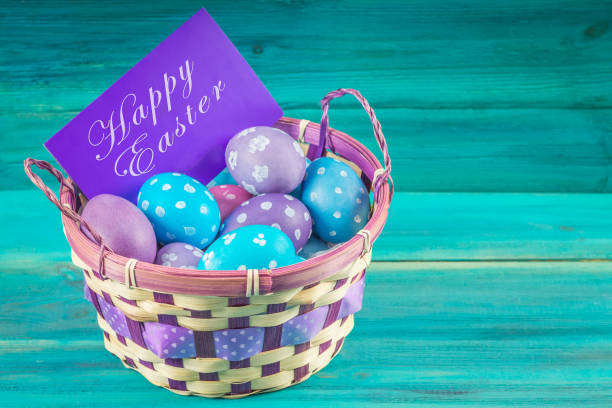 istock Violet and blue Easter eggs in a basket with a card. Blue wooden background. Happy easter. 864432478