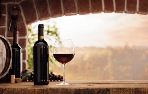 Red wine tasting in the cellar Red wine tasting in the wine cellar: wineglass and bottles next to the window and panoramic view of vineyards at sunset wine italian culture wine bottle bottle stock pictures, royalty-free photos & images