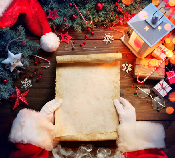 santa claus desk reading wish list with ornament and christmas gift - lista imagens e fotografias de stock