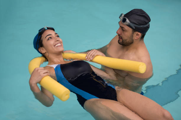 Woman taking a swimming lesson in the pool Woman taking a swimming lesson in the pool with a male instructor and learning how to float - lifestyle concepts women exercising swimming pool young women stock pictures, royalty-free photos & images