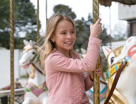 Happy positive preschool girl having a ride on the old vintage merry-go-round in city of St Malo France. Smiling child on a horse