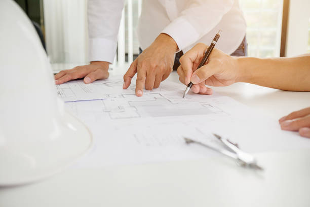 istock Architects engineer discussing at the table with blueprint - Closeup on hands and project print. 864458742