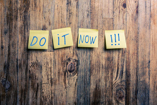 Do it now text on yellow post it notes attached to a wood background