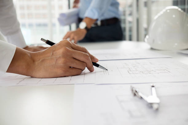 istock Architects engineer discussing at the table with blueprint - Closeup on hands and project print. 864458836