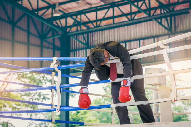 Defeated Asian businessman in suit with boxing in red gloves on boxing ring Defeated Asian businessman in suit with boxing in red gloves on boxing ring knockout stock pictures, royalty-free photos & images