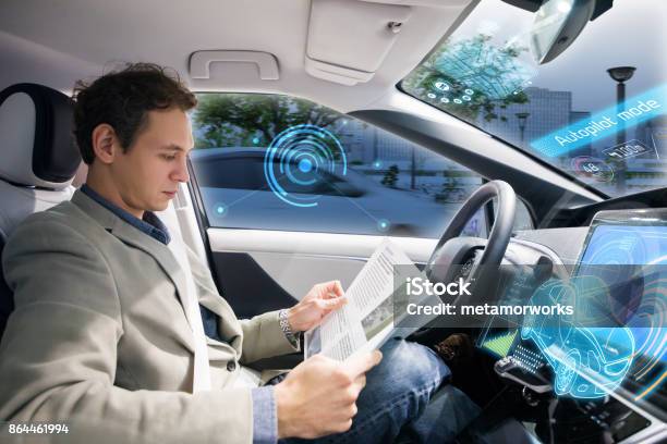 Caucasian Driver Reading Magazine In Autonomous Car Self Driving Vehicle Stock Photo - Download Image Now