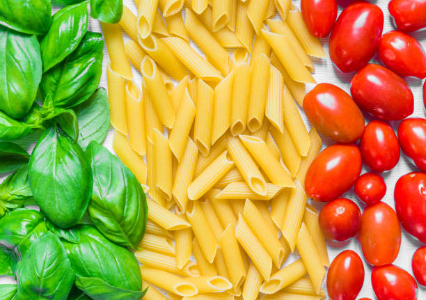 bunten nahrung hintergrund penne rigate nudeln, basilikum und kirschtomaten in form der italienischen flagge - penne rigatoni pasta tomato pasta stock-fotos und bilder