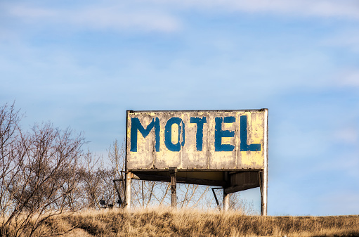 A vintage blue and yellow peeling painted MOTEL sign on a brown grassy hilltop in a autumn landscape