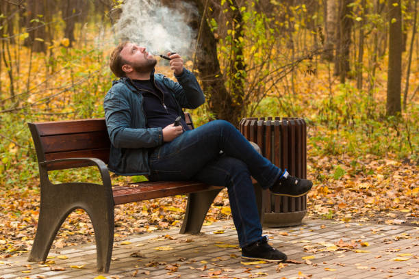 istock Young man smokes tobacco pipe in park 864475458