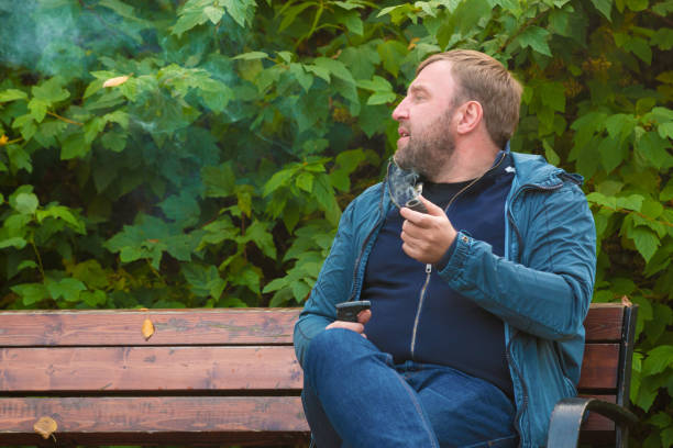 istock Young man smokes tobacco pipe in park 864475488
