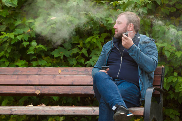 istock Young man smokes tobacco pipe in park 864475490