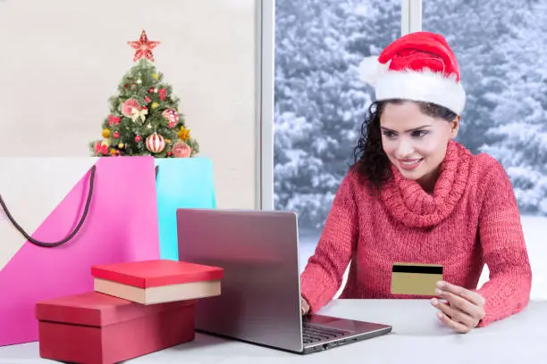 Pretty girl using a laptop while holding a credit card for shopping online and sitting at home
