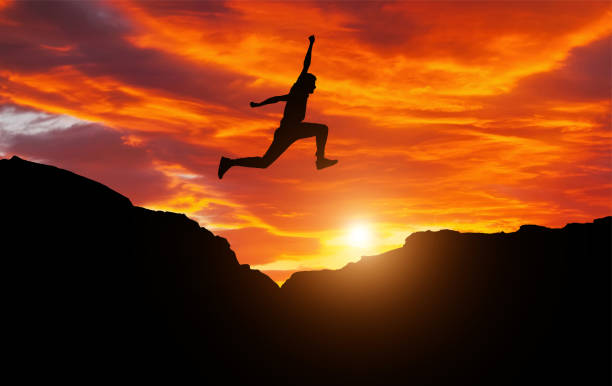 silueta del atleta, saltando sobre las rocas en la zona de la montaña contra la puesta de sol. entrenamiento correr y saltar en condiciones difíciles en una hermosa naturaleza con cielo nublado - unstoppable fotografías e imágenes de stock