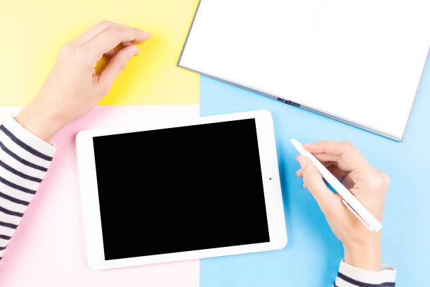 istock Female hands with pen, open notebook and tablet computer over yellow, blue and pink background 864479416