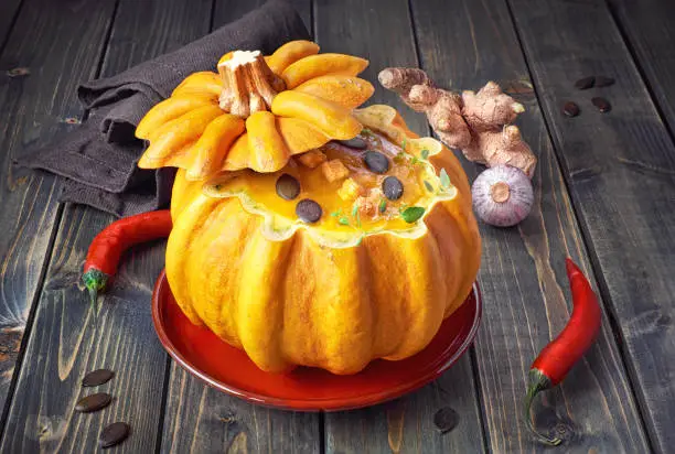 Spicy pumpkin soup served on a dark wood  in a hollowed pumpkin with croutons, pumpkin seeds and thyme
