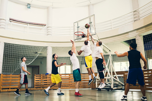 Friends Playing Basketball in a school gym. One player about to do slam dunk during basketball game in basketball court.
