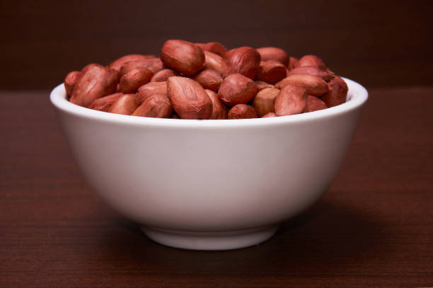 Peanuts in a white bowl. Background of a dark tree.