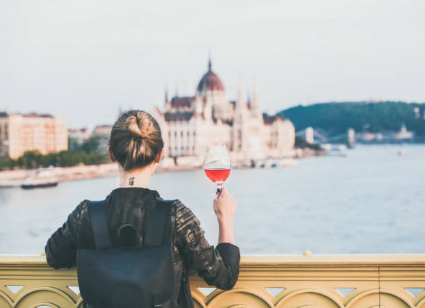 Young woman standing with glass of rose wine in Budapest Young woman tourist standing with glass of rose wine at Margaret bridge in Budapest, Hungarian Parliament building and Duna river at background hungarian culture stock pictures, royalty-free photos & images