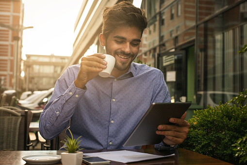 Sonriente hombre de negocios sentado en la calle cafetería tomando café y el uso de iPod. photo