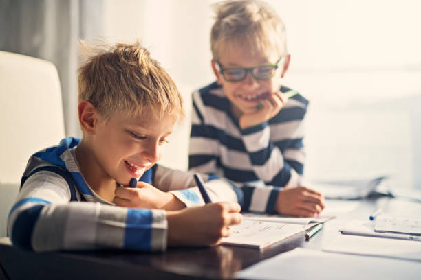 hermanos que se divierten haciendo la tarea juntos - twin tips fotografías e imágenes de stock