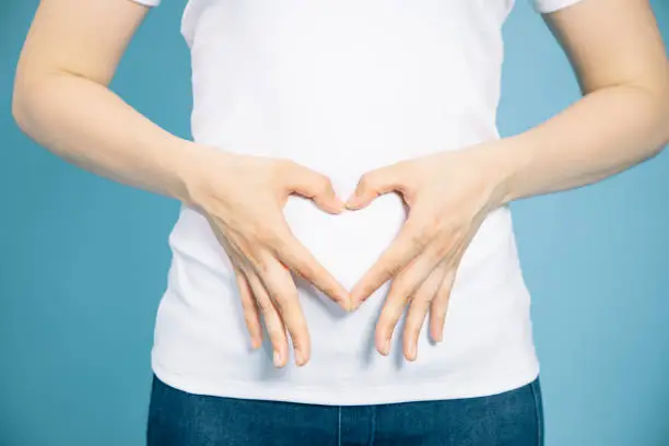 young woman who makes a heart shape by hands on her stomach.