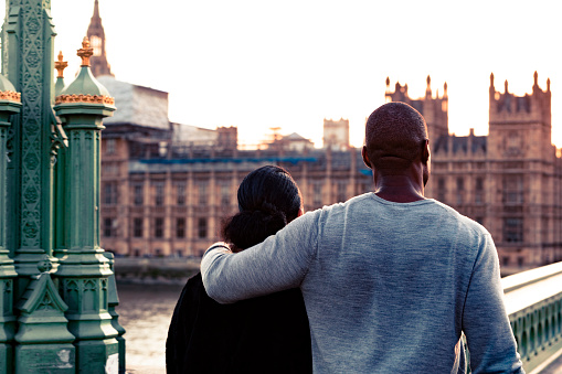 Young couple walking together past Big Ben in the evening. Seen from behind, as they walk towards parliament.