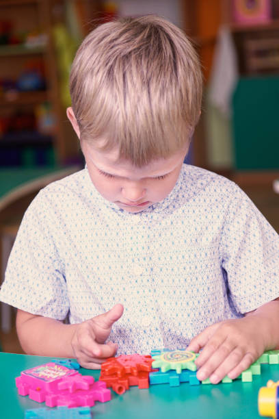 istock Little frustrated boy playing with colorful plastic bricks at the table in the kindergarten. 864504372