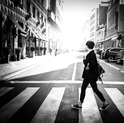 Black and white photo of young man crossing the city street watching away from the camera to do sun.