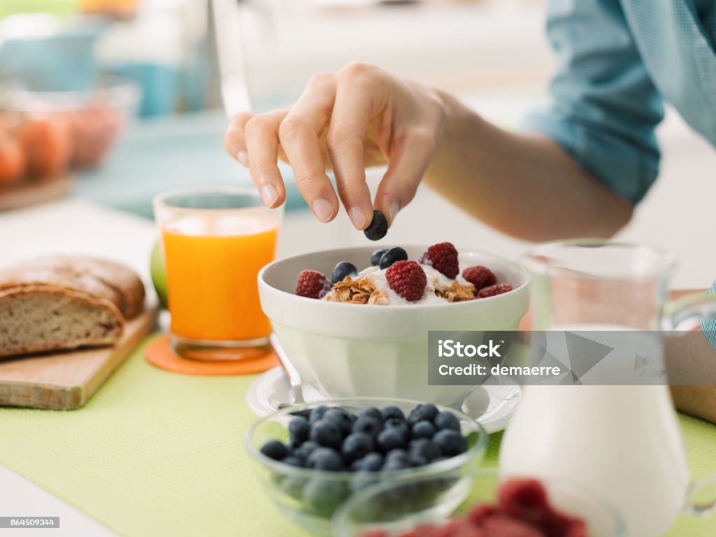 Healthy breakfast at home Woman having an healthy delicious breakfast at home with yogurt, cereals and fresh fruit, she is picking a blueberry Breakfast Stock Photo