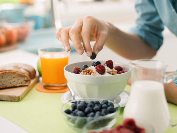 Healthy breakfast at home Woman having an healthy delicious breakfast at home with yogurt, cereals and fresh fruit, she is picking a blueberry breakfast stock pictures, royalty-free photos & images