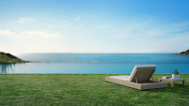piscine vue de mer à côté de la terrasse et lit dans la maison de plage de luxe moderne avec le fond de ciel bleu, chaise de salon sur l’herbe verte à la maison de vacances ou hôtel - green sky water wave photos et images de collection