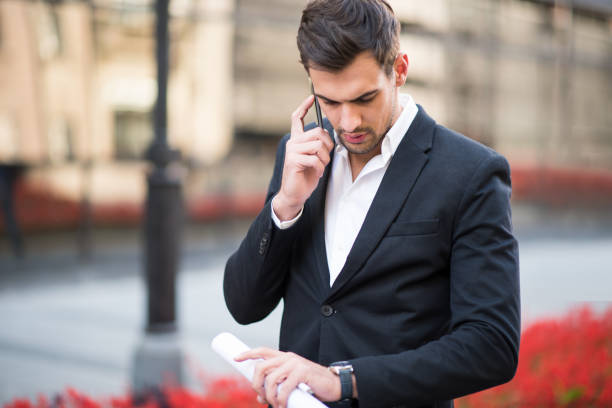 istock Businessman talking on a mobile phone and holding rolled up documents 864526578