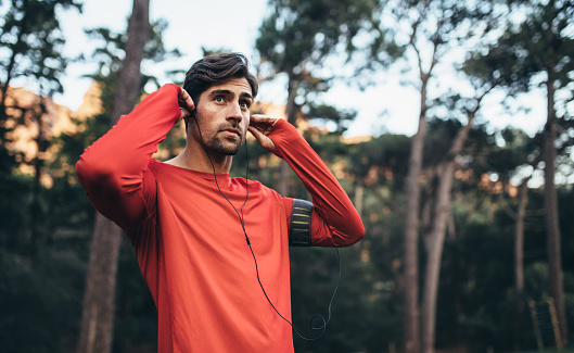 Man wearing earphones looking away. Runner listening to music during morning jog.