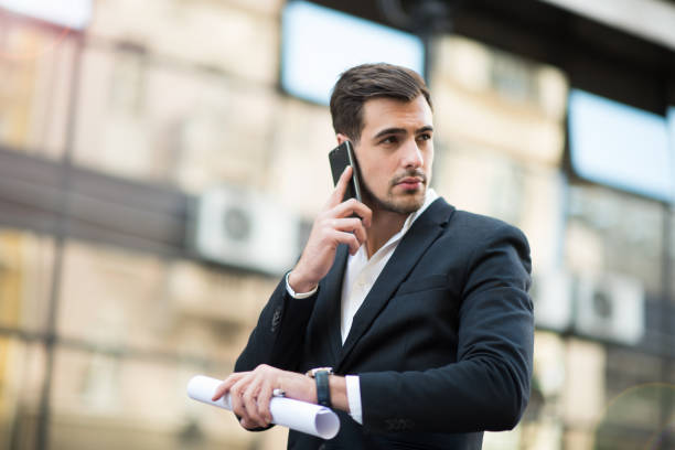 istock Businessman talks on a mobile phone and holds rolled up documents 864527450