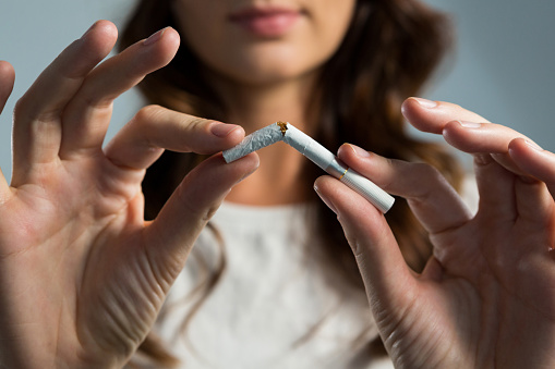 Mid section of woman breaking cigarette against white background