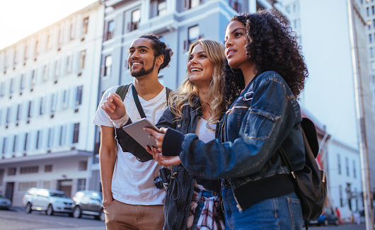 Tourists using navigation tools to explore the city. Man with two women friends exploring the city with travel accessories.